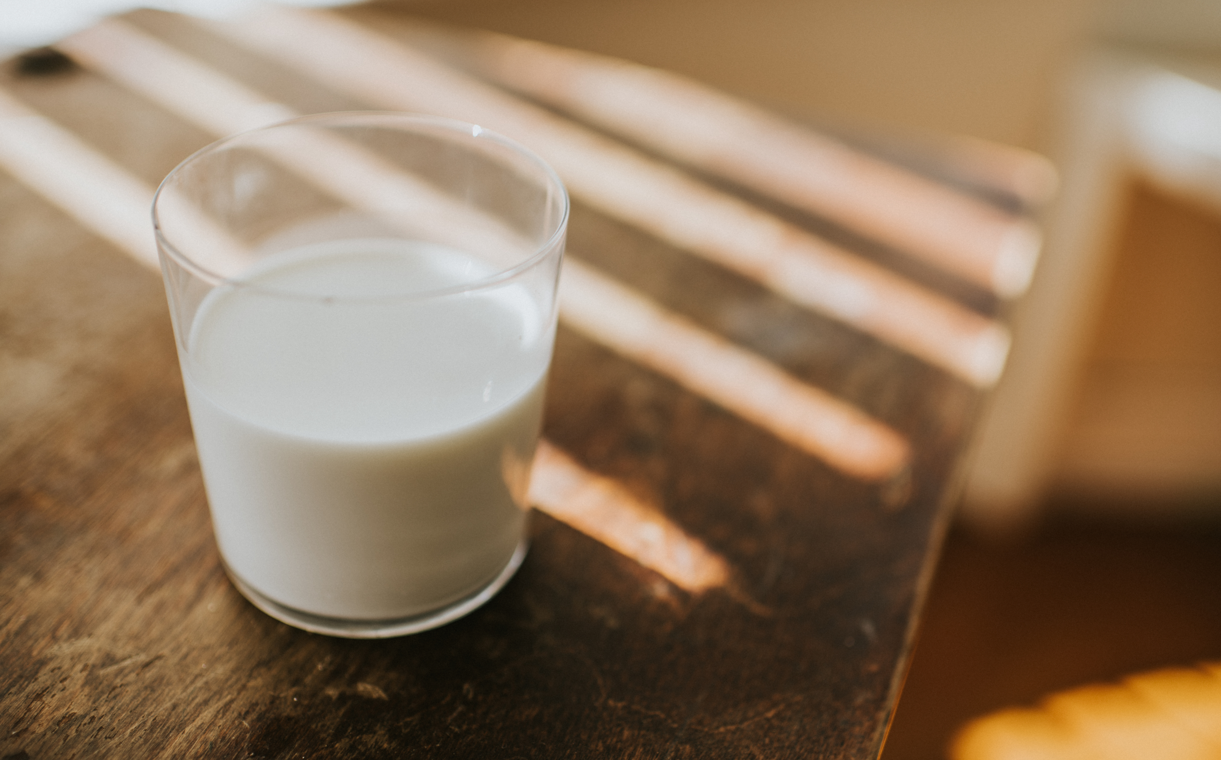 Glass of milk on a wooden table with sunlight casting shadows