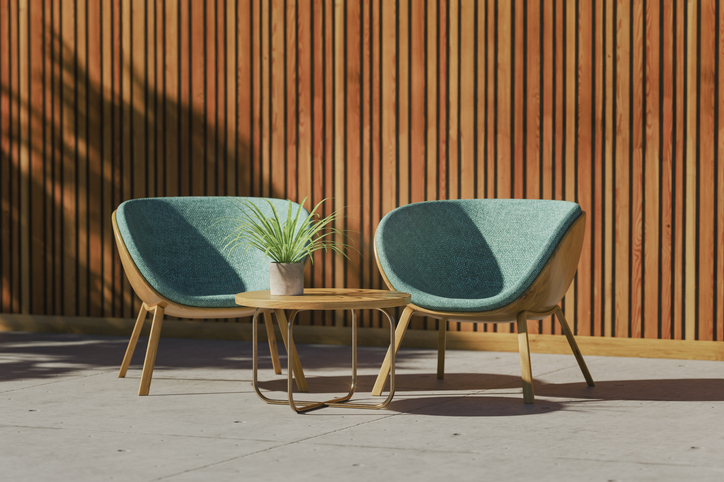 Two modern chairs with a small table and plant between them, in front of a wood slat wall