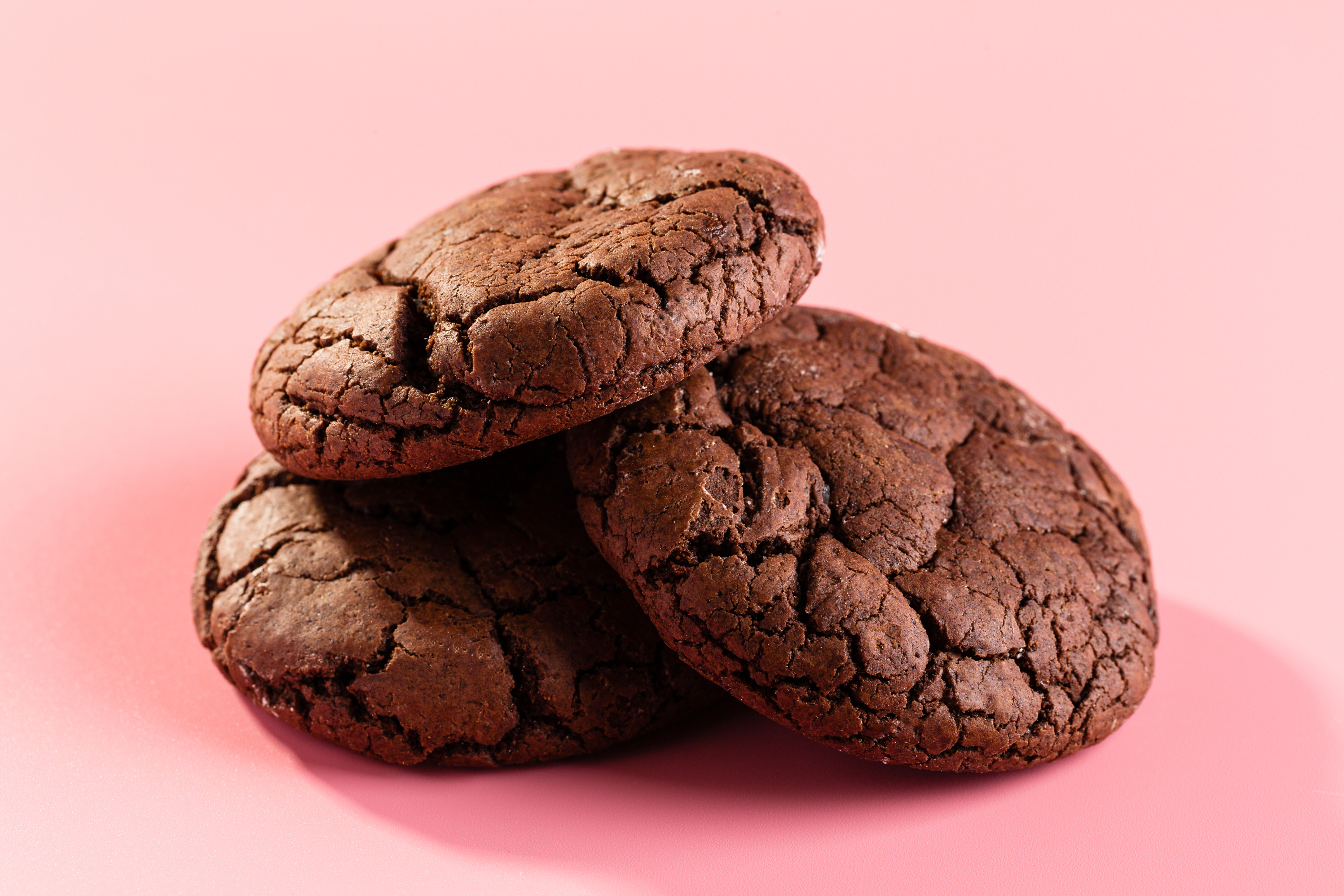 Three chocolate cookies stacked on a plain surface