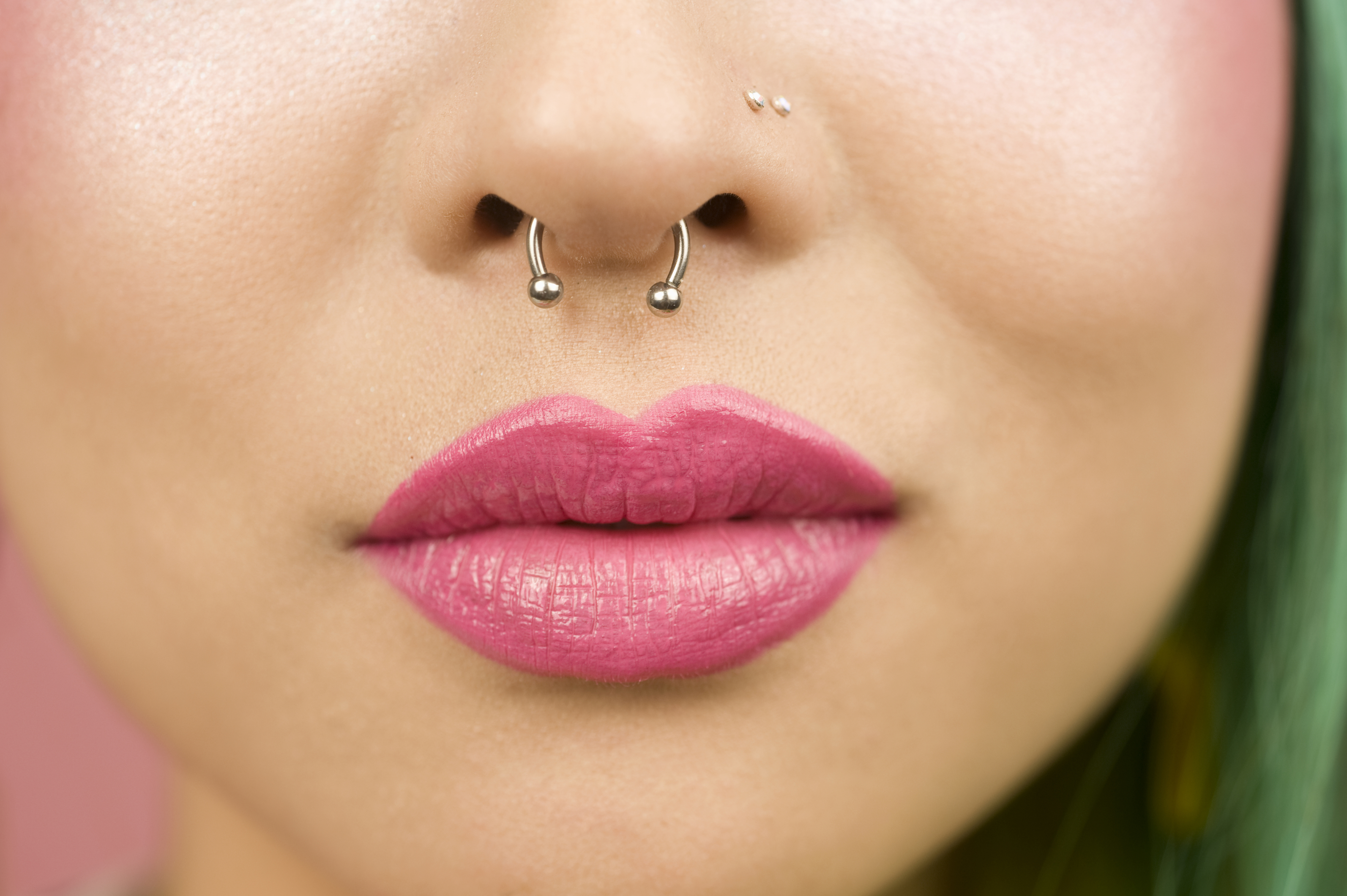 Close-up of a person&#x27;s lips slightly parted, wearing pink lipstick and a septum nose piercing