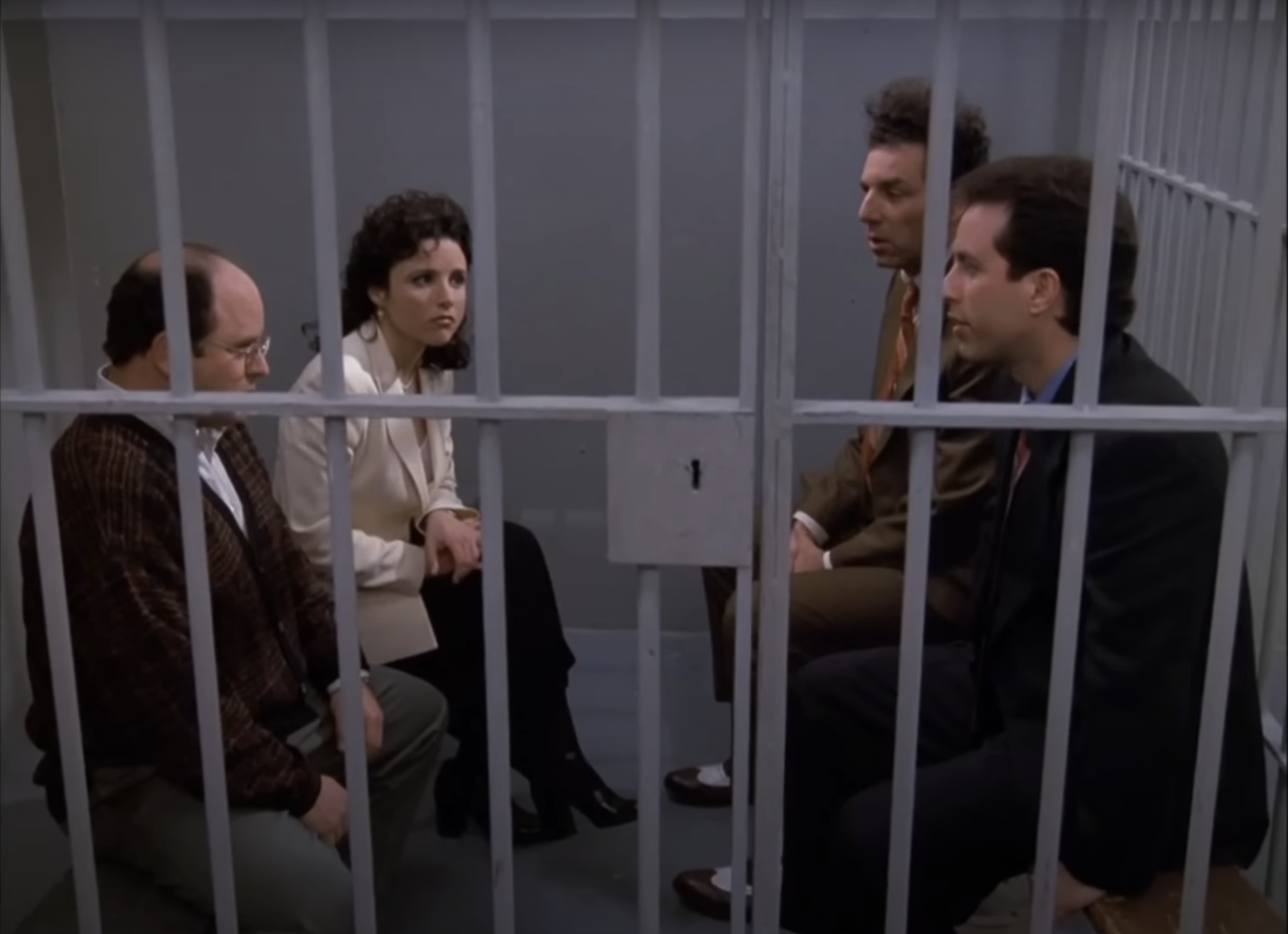 Four characters from &quot;Seinfeld&quot; sit in a jail cell, with expressions ranging from concerned to indifferent