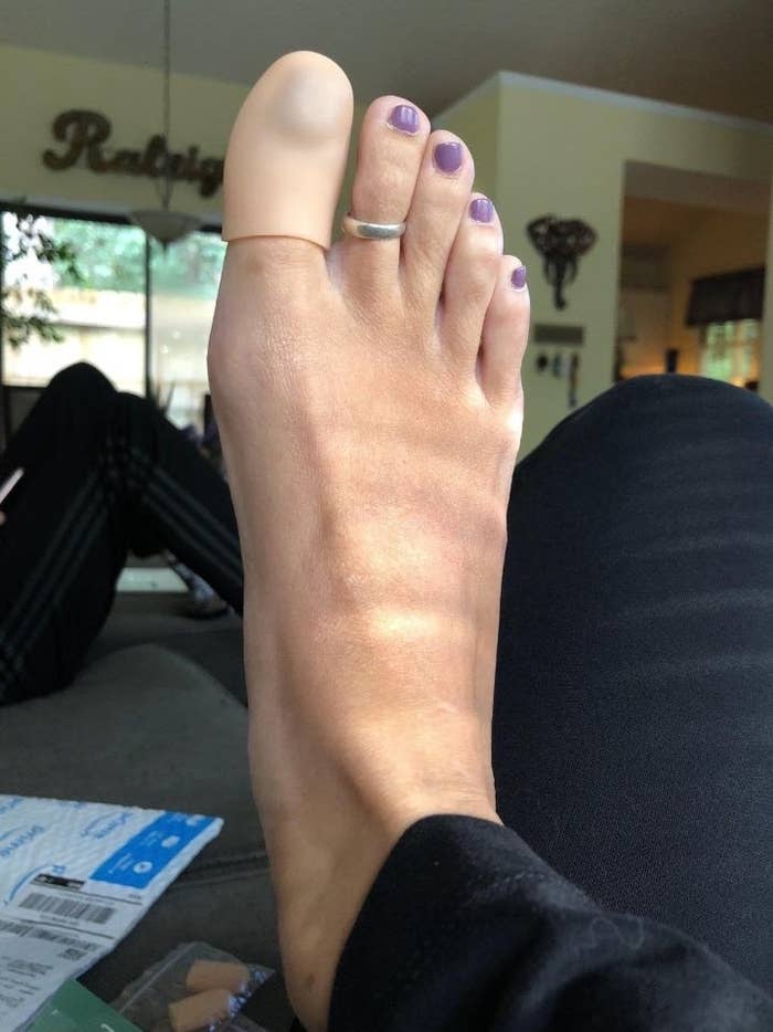 A person&#x27;s bare foot with a toe ring and purple nail polish, resting indoors near printed materials