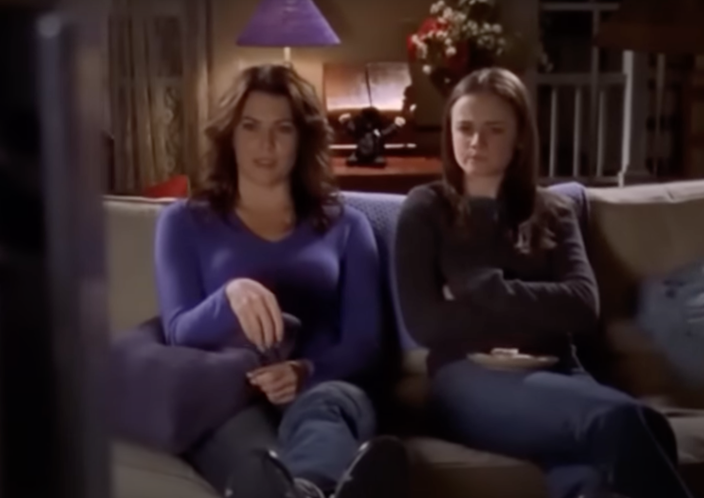 Lorelai and Rory from Gilmore Girls sit on couch, Lorelai in a casual top, Rory in a sweater