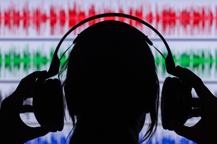 Silhouette of a person with headphones against a background of audio waveform graphics