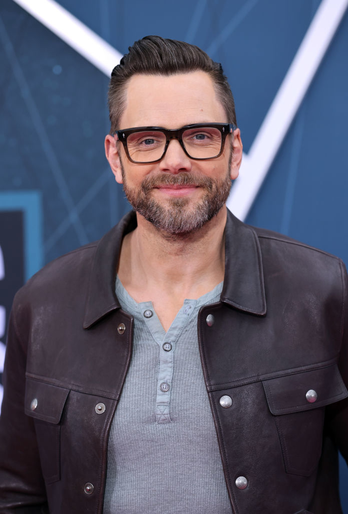 closeup of joel in a leather jacket and glasses smiling at the camera