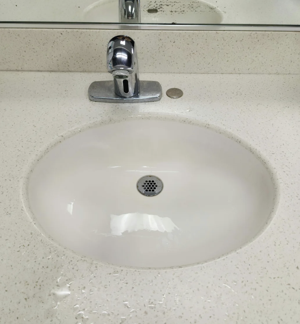 Close-up of a white, oval bathroom sink with a chrome faucet, reflecting overhead lighting