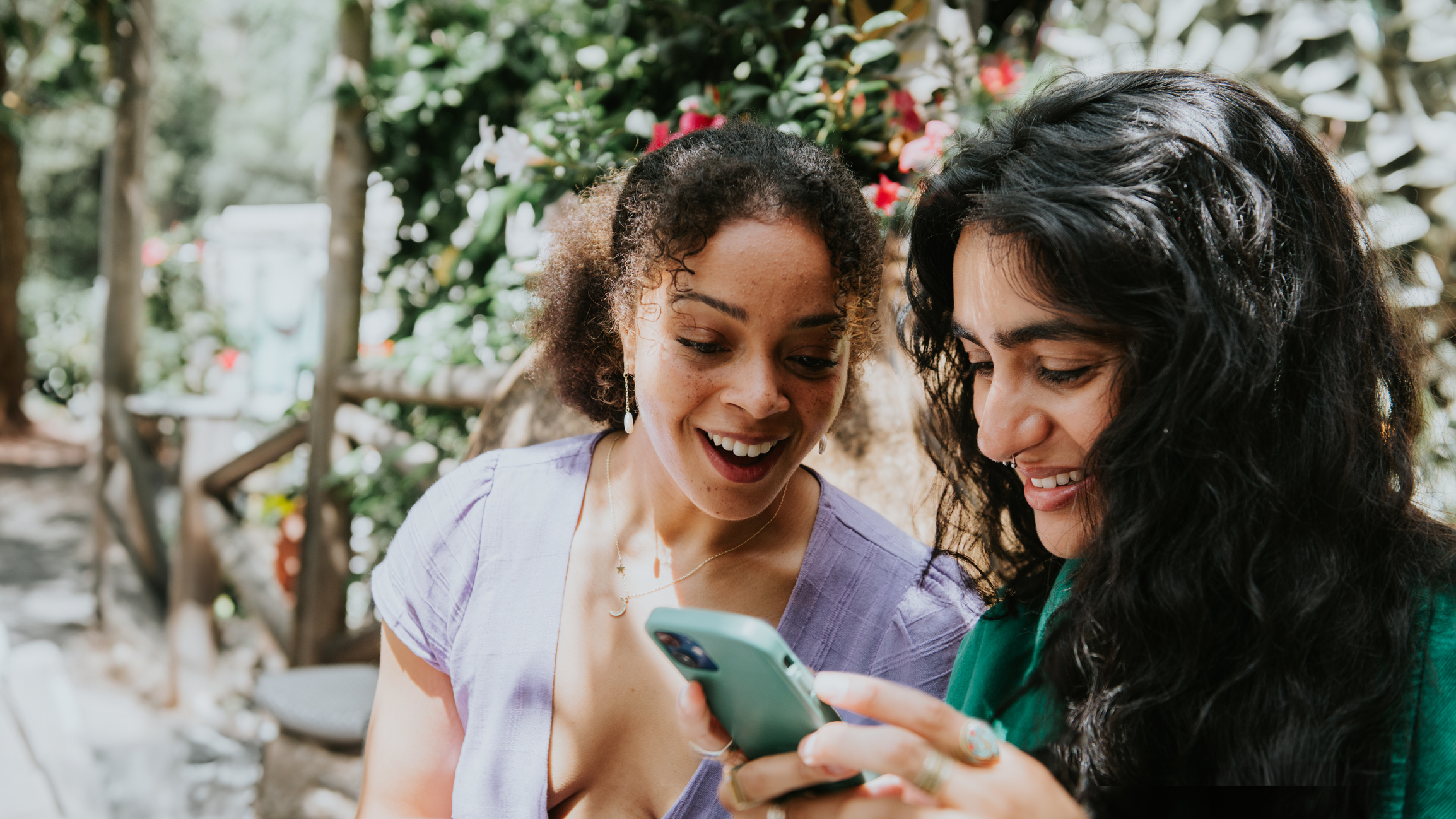 Two women smiling and looking at a smartphone together outdoors