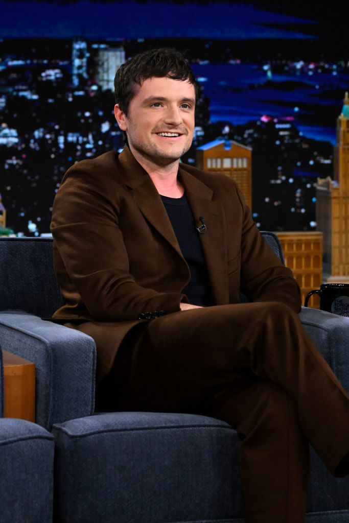 josh in suit sitting with crossed legs on a talk show set