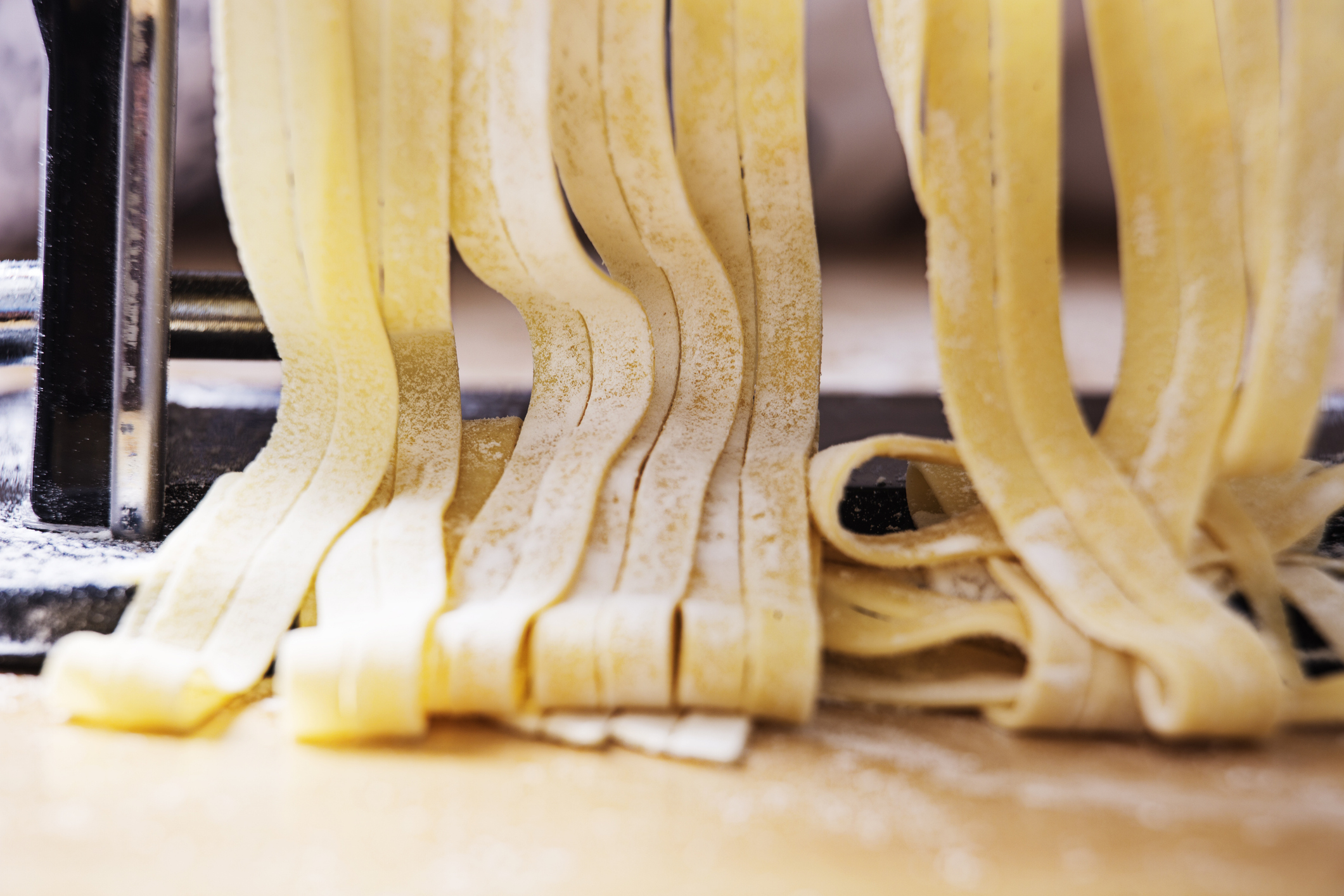 Fresh pasta dough being cut into noodles by a pasta machine