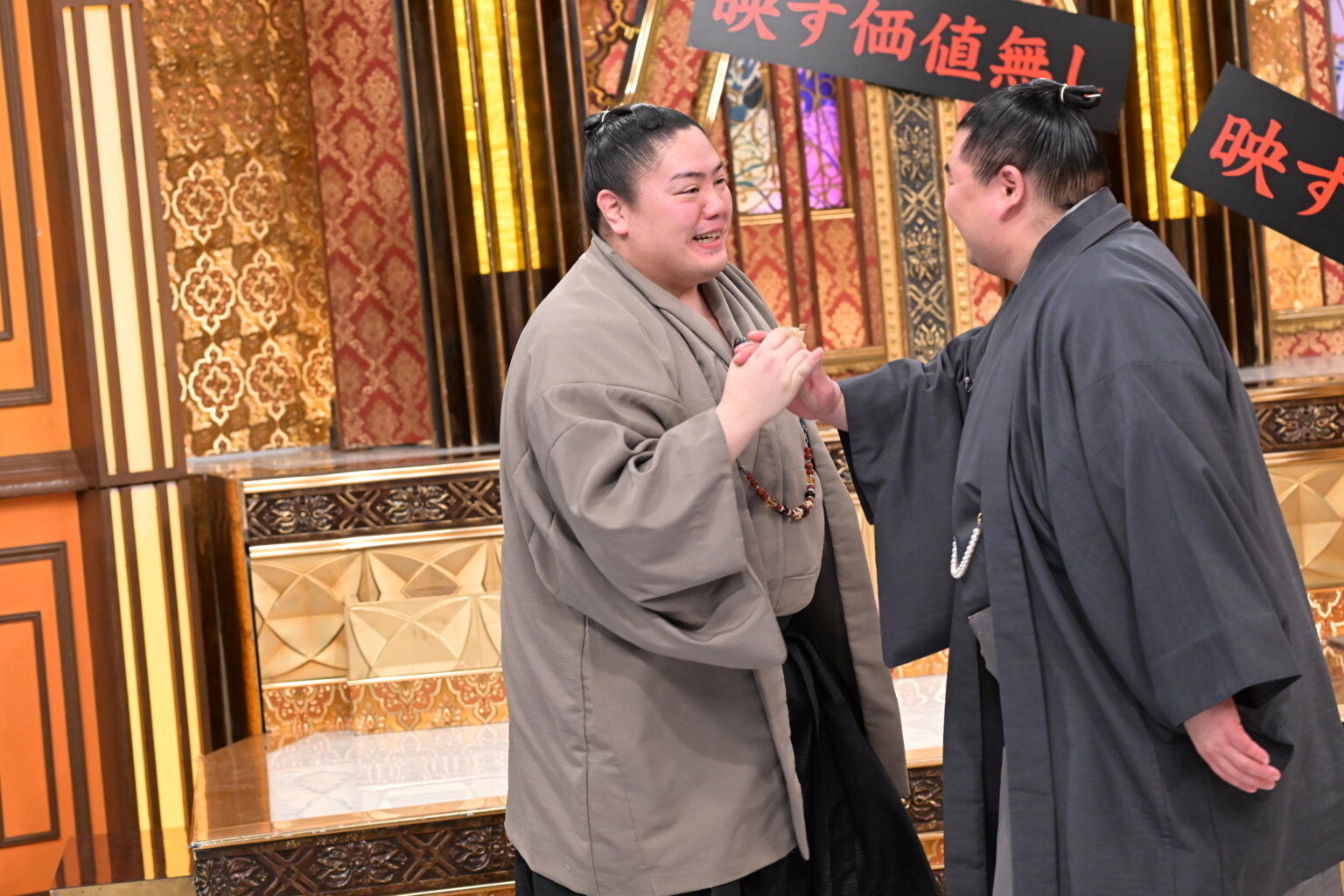 二人の相撲レスラーが和服を着て握手している。