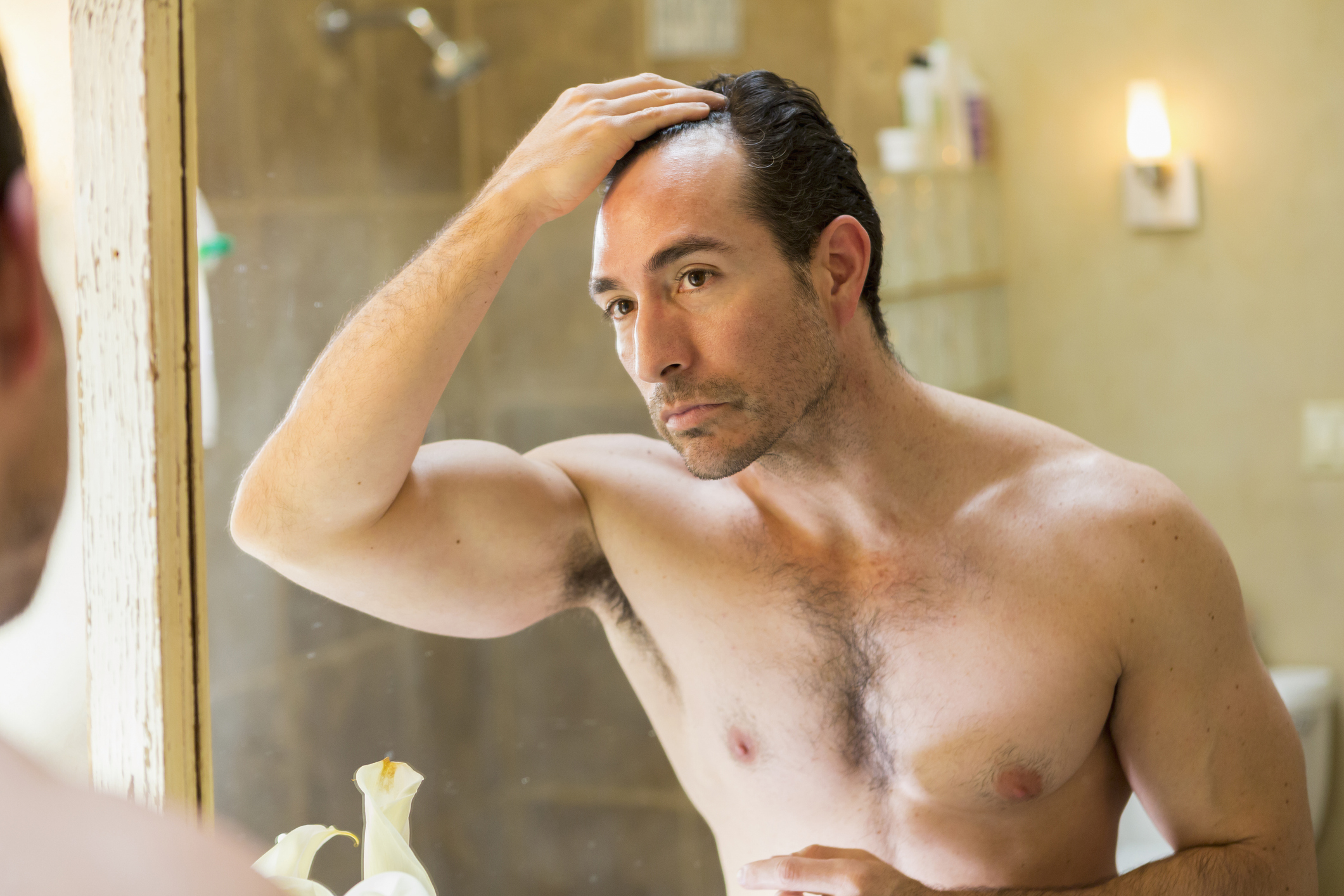 Man examining his hairline in the mirror, concerned expression, in a bathroom setting