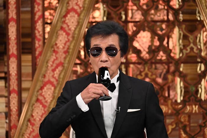 黒のタキシードを着た男性がマイクで話している。