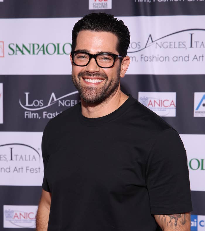 Jesse Metcalfe posing in a black t-shirt and beige trousers at an event