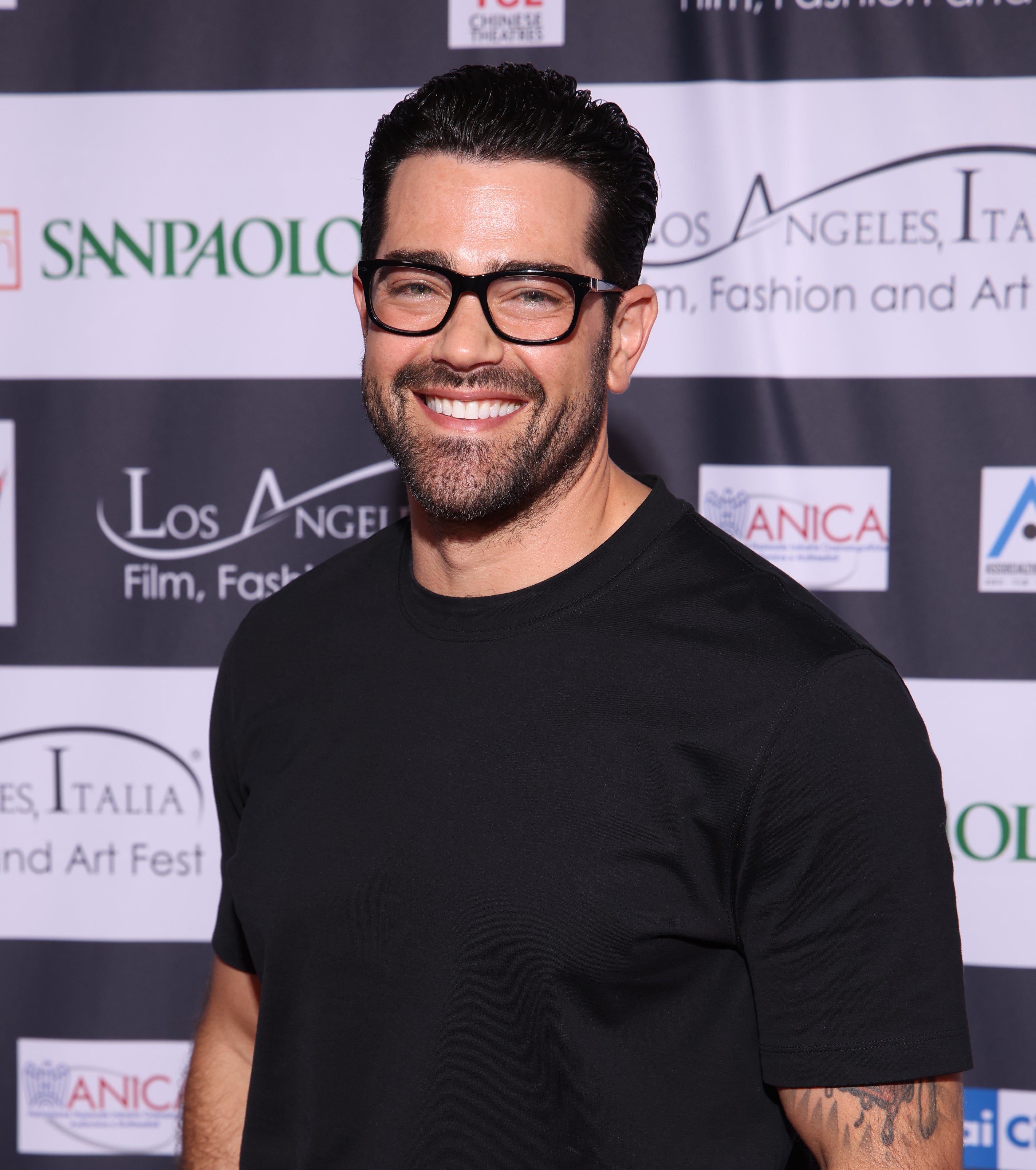 Jesse Metcalfe posing in a dark t-shirt and beige trousers at an event