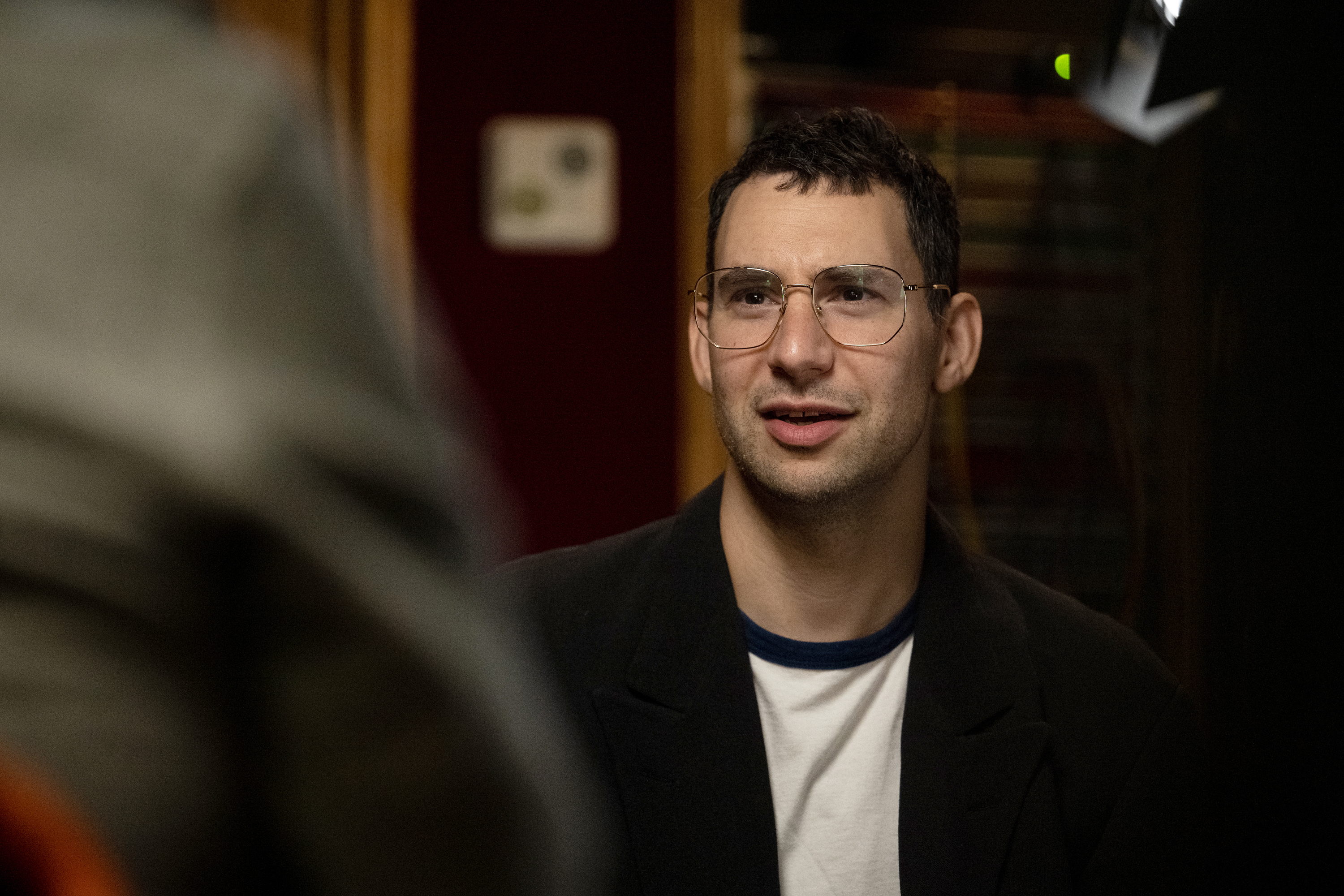 Jack in glasses and casual attire speaking with an out-of-focus person in the foreground