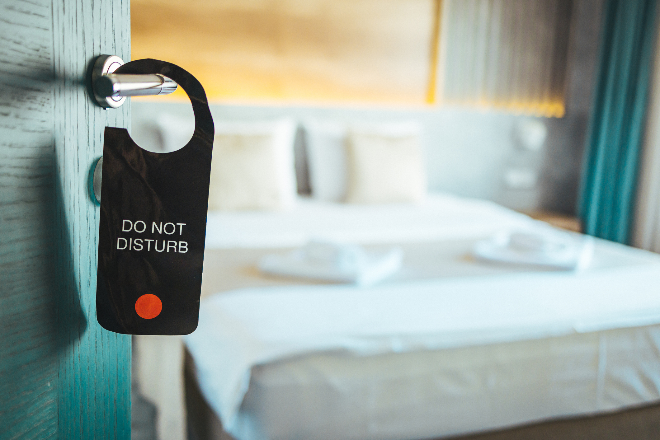 Do Not Disturb sign hung on a hotel room door with a blurred bed in the background