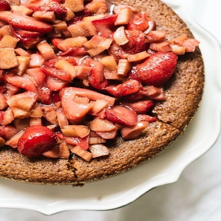 Close-up of a cake topped with chopped strawberries and rhubarb on a white plate