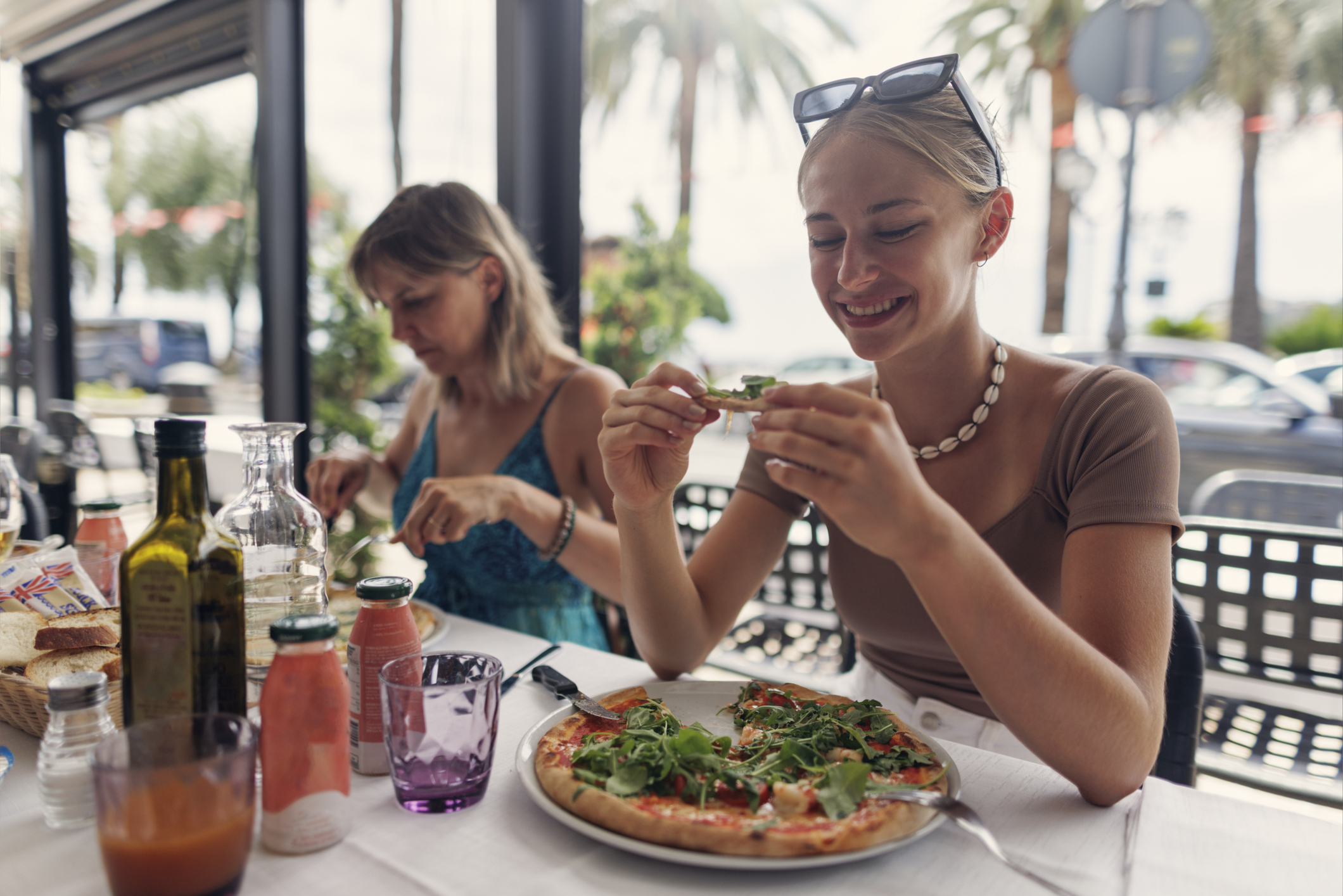 Woman enjoying a pizza at an outdoor restaurant with another person in the background