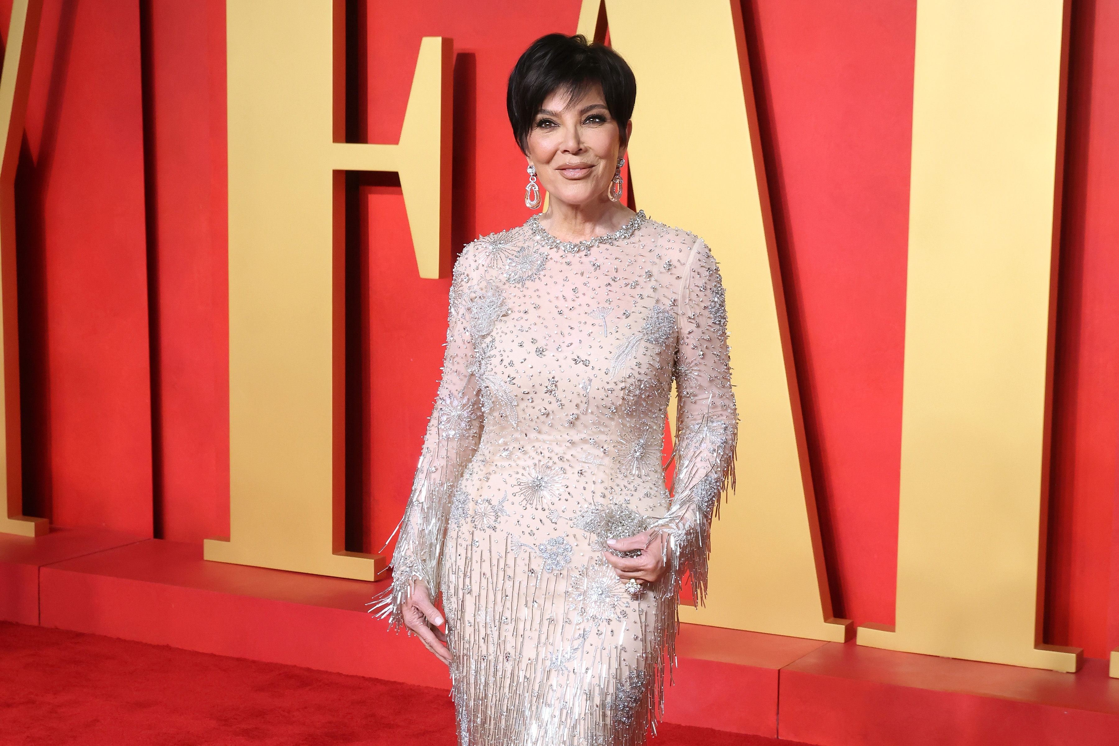 Kris Jenner in an embellished long-sleeve gown with fringe details posing on the red carpet
