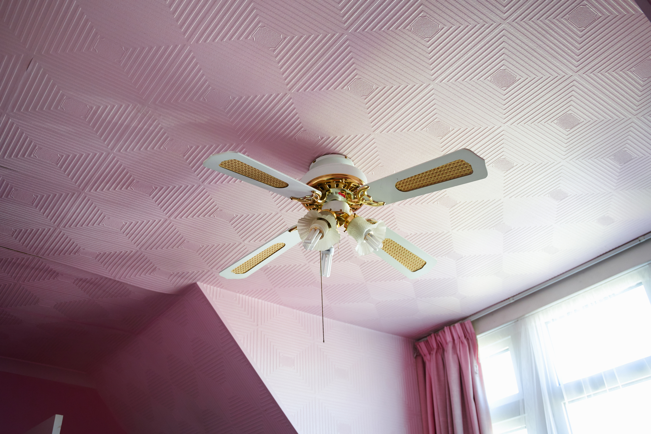 Ceiling fan with light fixture attached, mounted on a textured ceiling, near a window with pink curtains