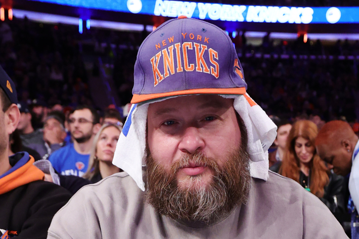 Person at a sports event wearing a Knicks hat; excitement in the background