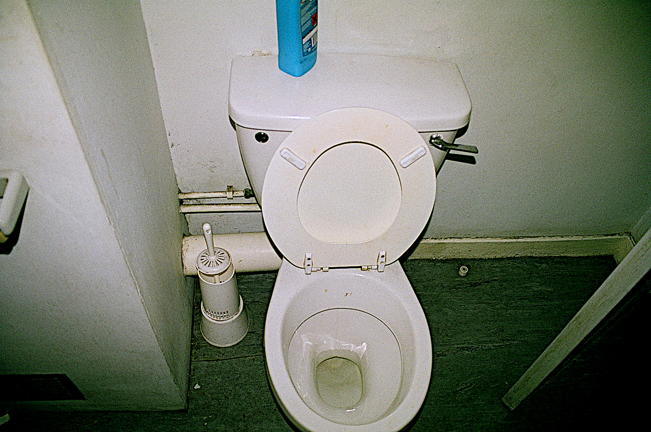 A toilet with an open lid and a brush beside it in a bathroom