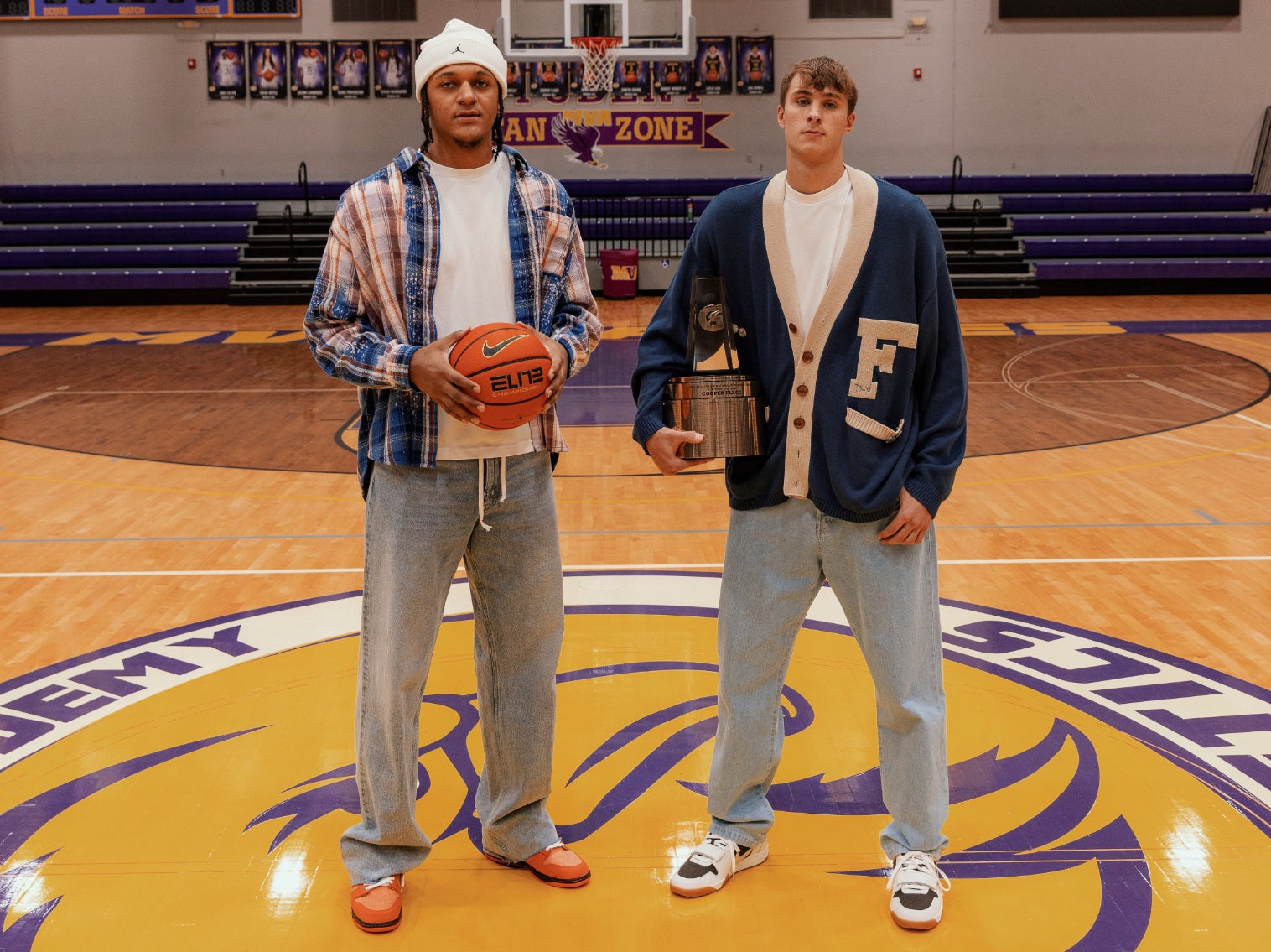 Two individuals standing on a basketball court, one holding a basketball, both wearing casual attire with prominent lettering