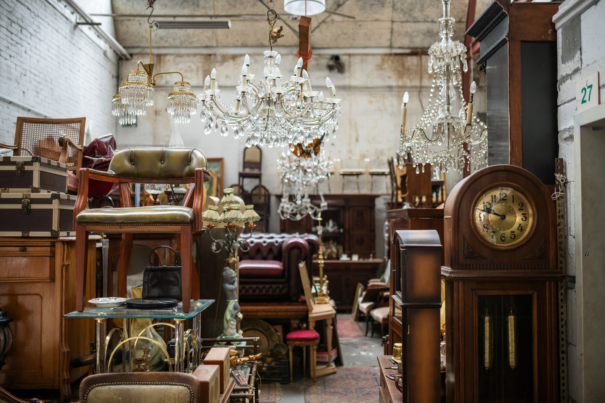 An antique shop interior with various furniture items, chandeliers, and a grandfather clock