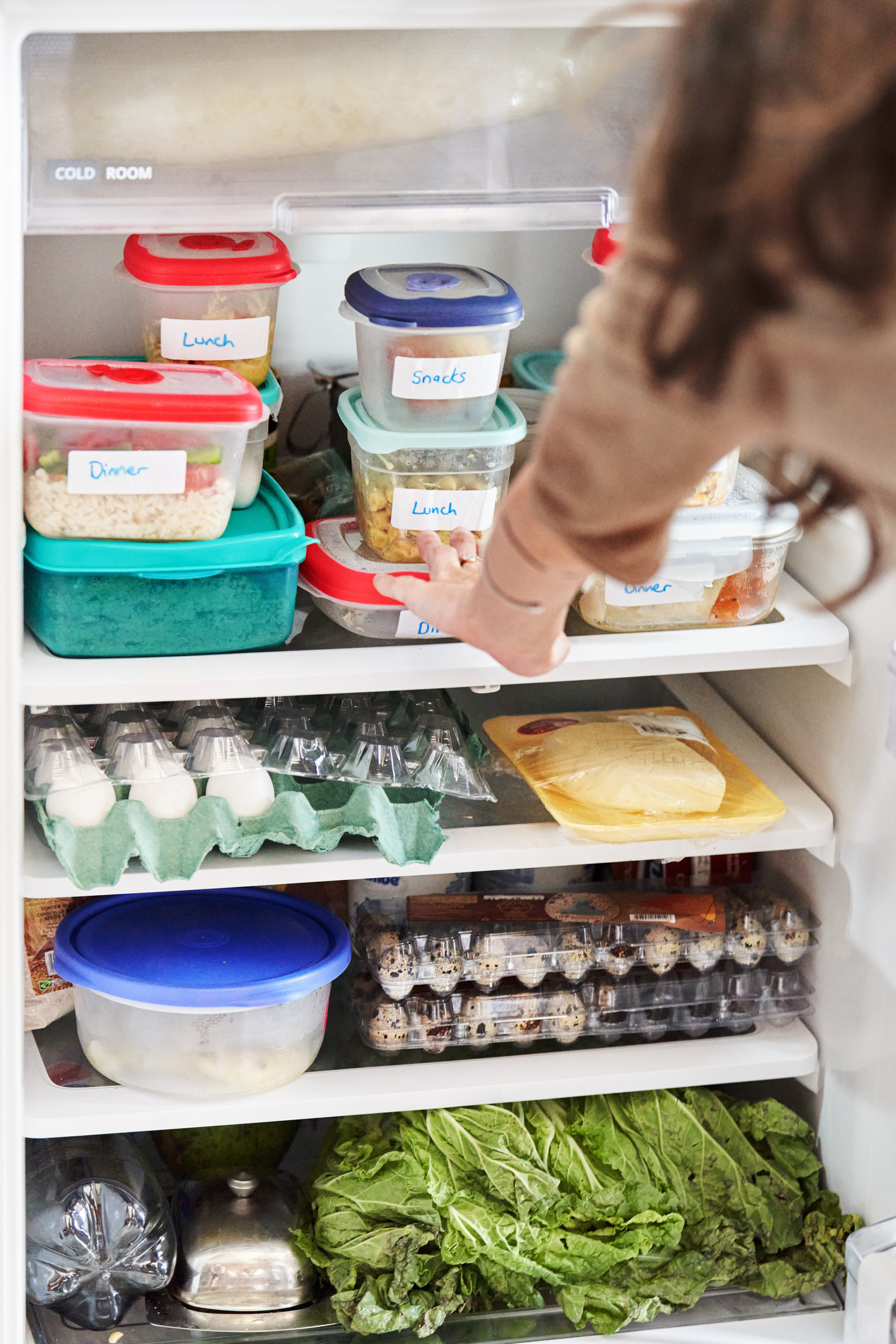 Person reaching into a fridge stocked with labeled containers and fresh produce
