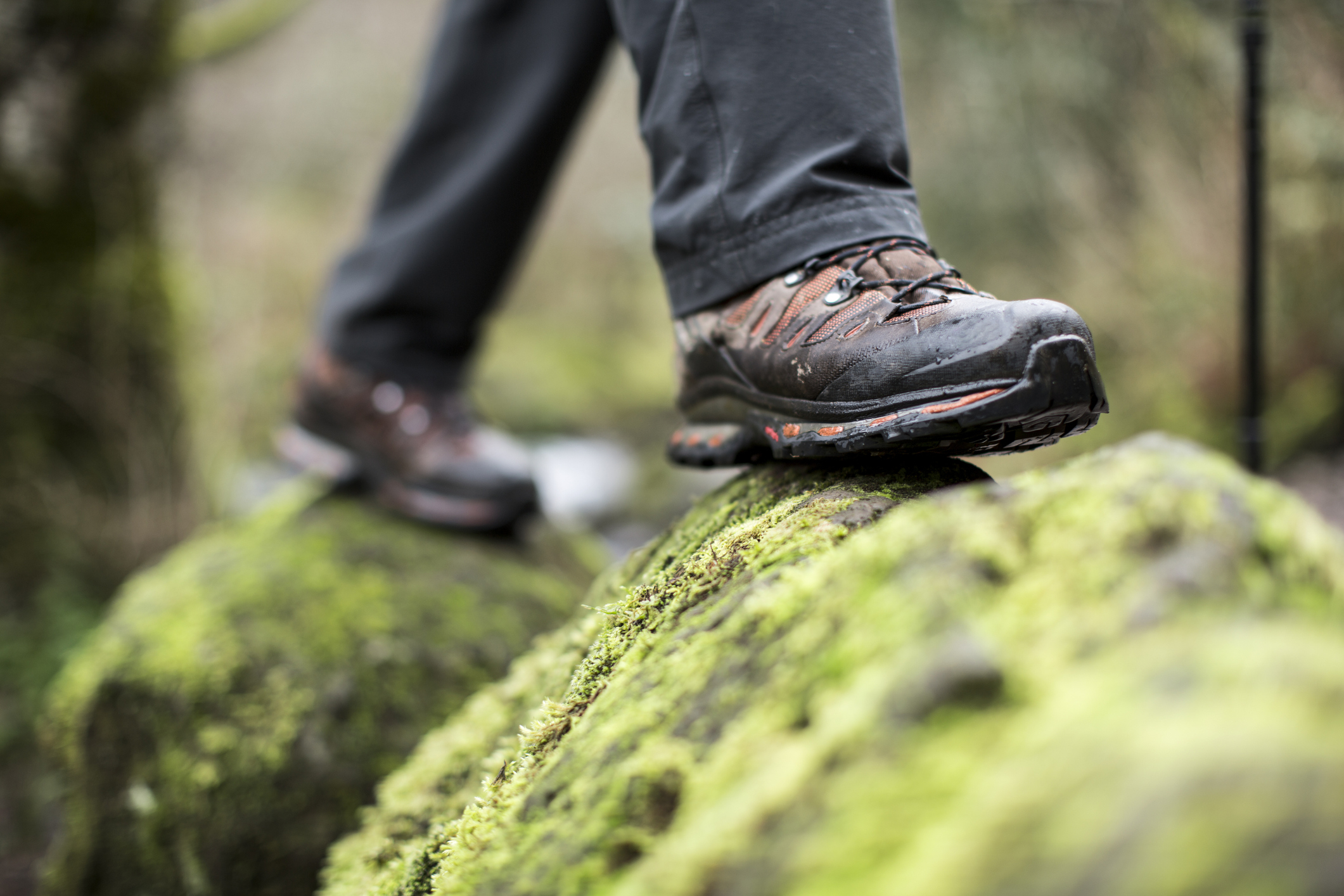 Close-up of a person&#x27;s feet in hiking boots balancing on a mossy rock