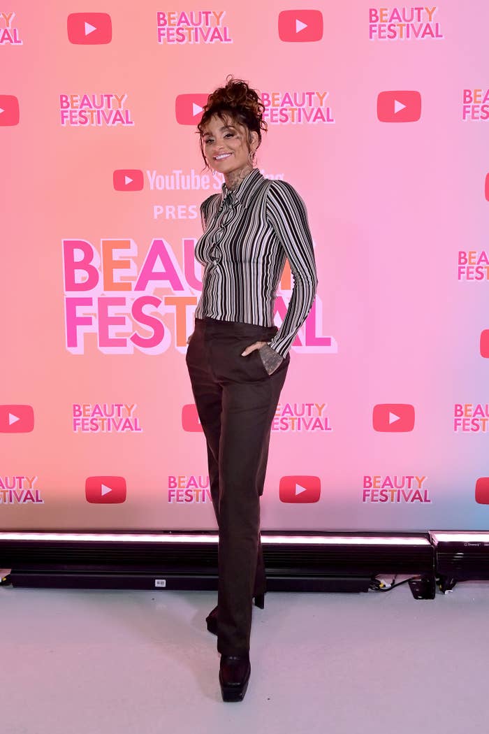 Woman posing at Beauty Festival with striped shirt and brown trousers, hands on hips