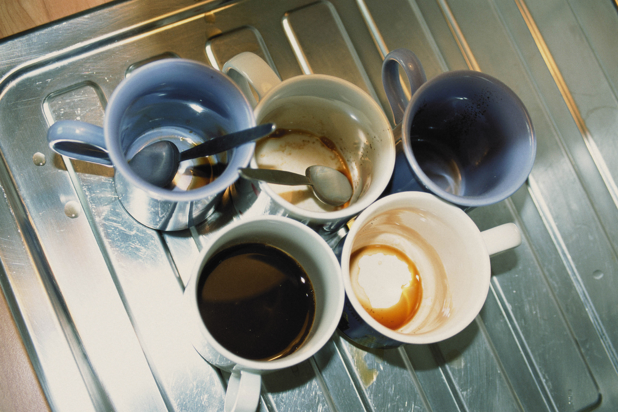 Four used coffee cups with spoons on a tray, one cup with leftover coffee