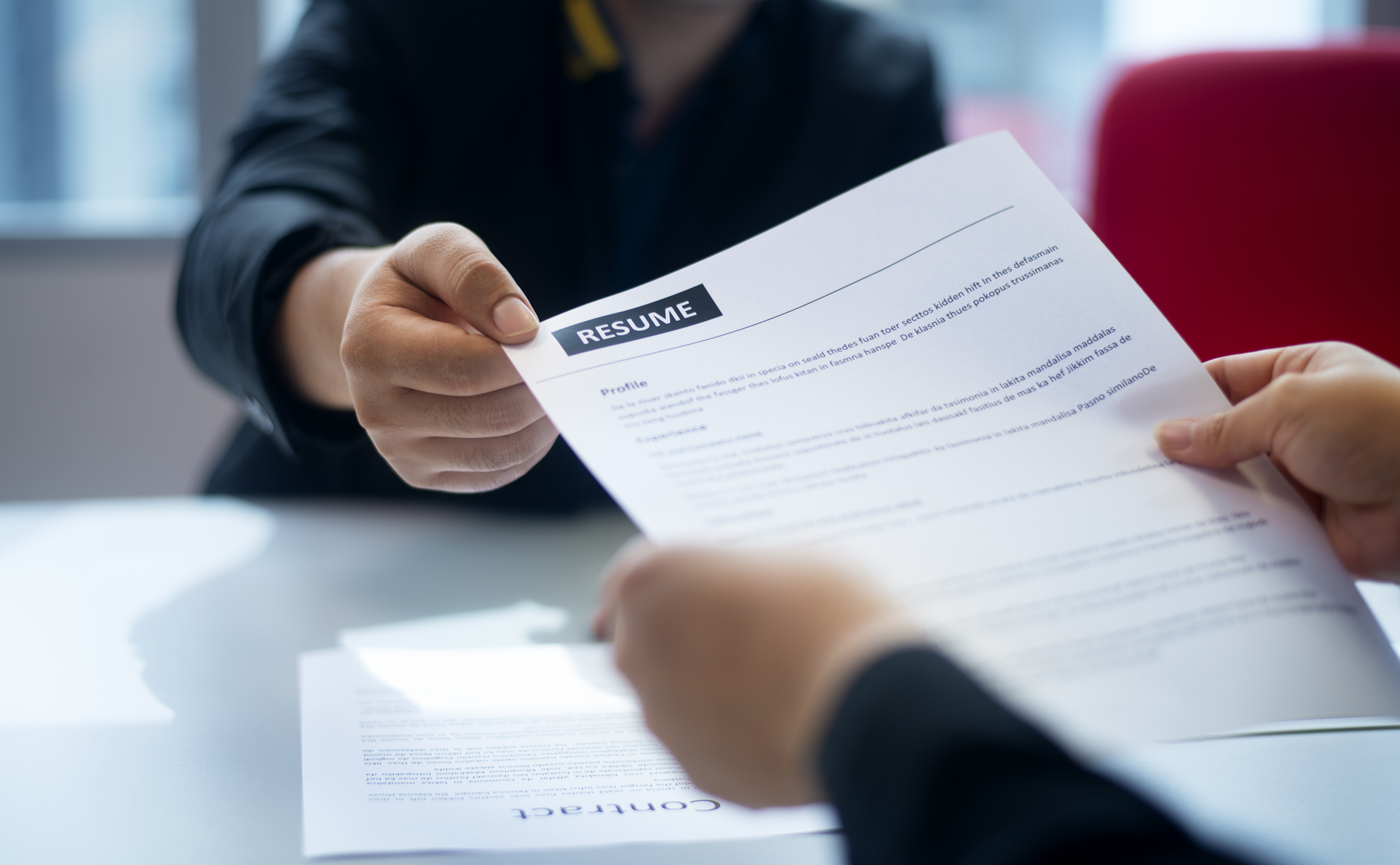 Hands exchanging a résumé across a desk during a job interview