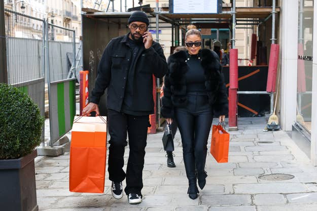 Two individuals in stylish winter attire with shopping bags walking side by side