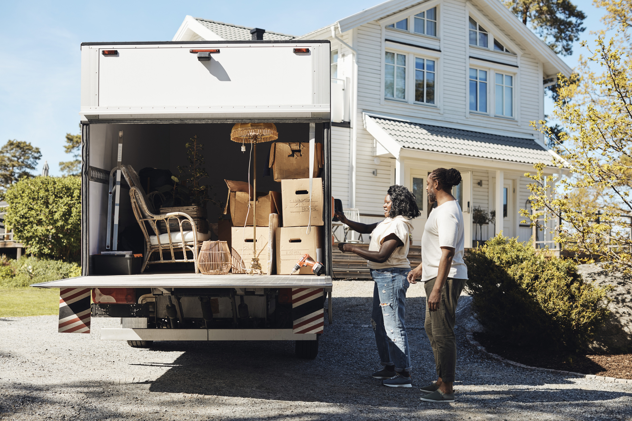 Two people standing beside a moving truck, packed with furniture and boxes, in front of a house