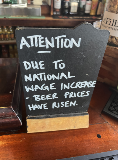 Sign reading &quot;ATTENTION DUE TO WAGE INCREASE - BEER PRICES HAVE RISEN&quot; on a bar counter