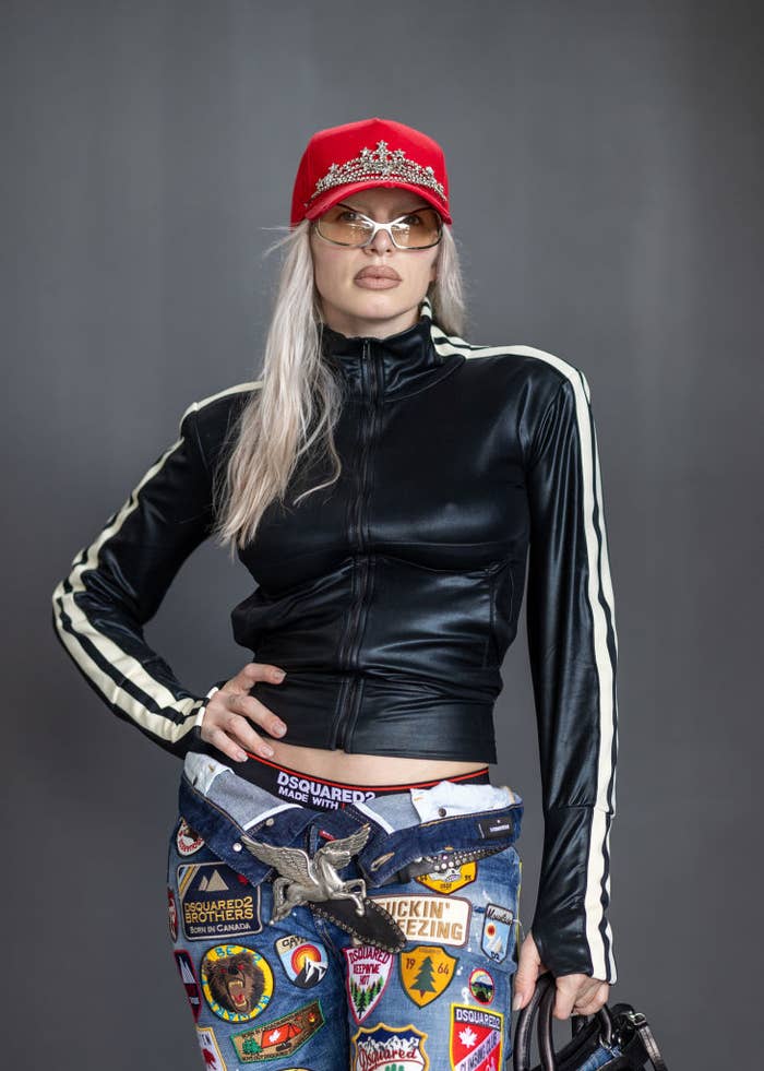 julia in a sporty black top and embellished jeans with patches, wearing a cap and sunglasses, posing confidently