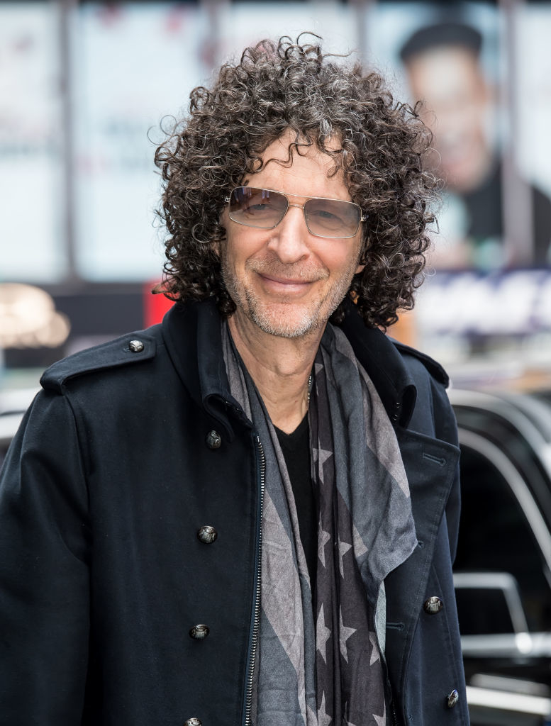 howard with curly hair wearing a black coat and patterned scarf, smiling at the camera