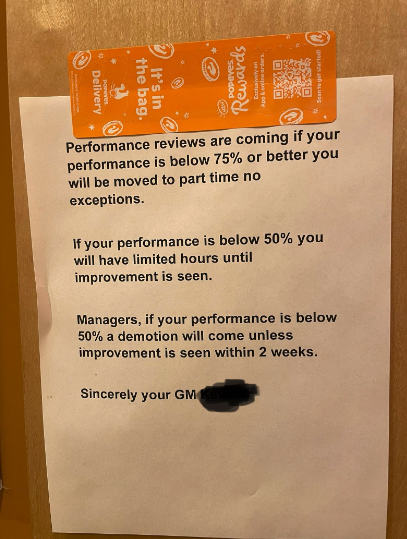 Notice on door about performance reviews, stating potential demotion if performance is below certain thresholds, signed by GM