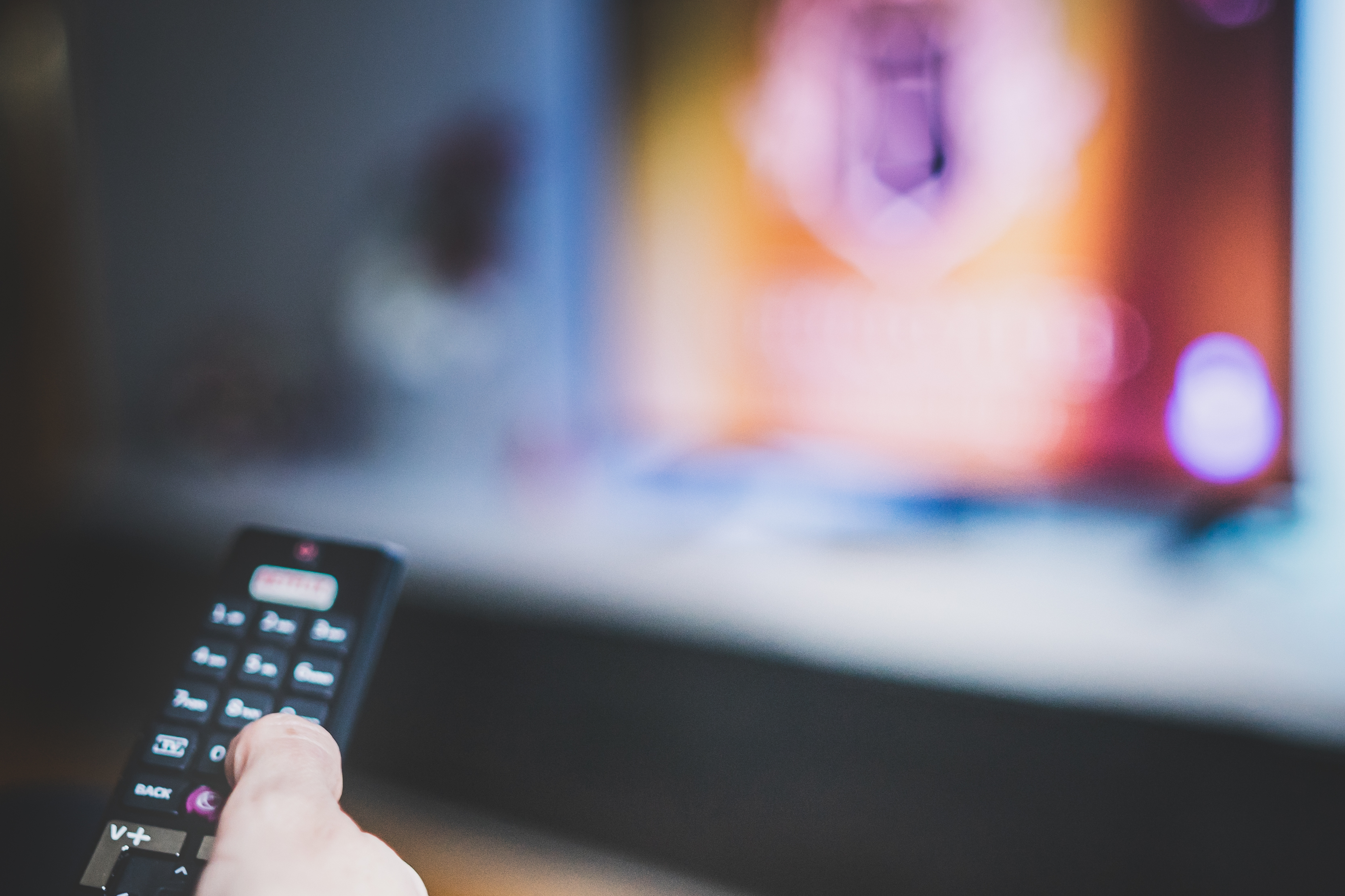 Person holding a remote, blurry TV screen in the background