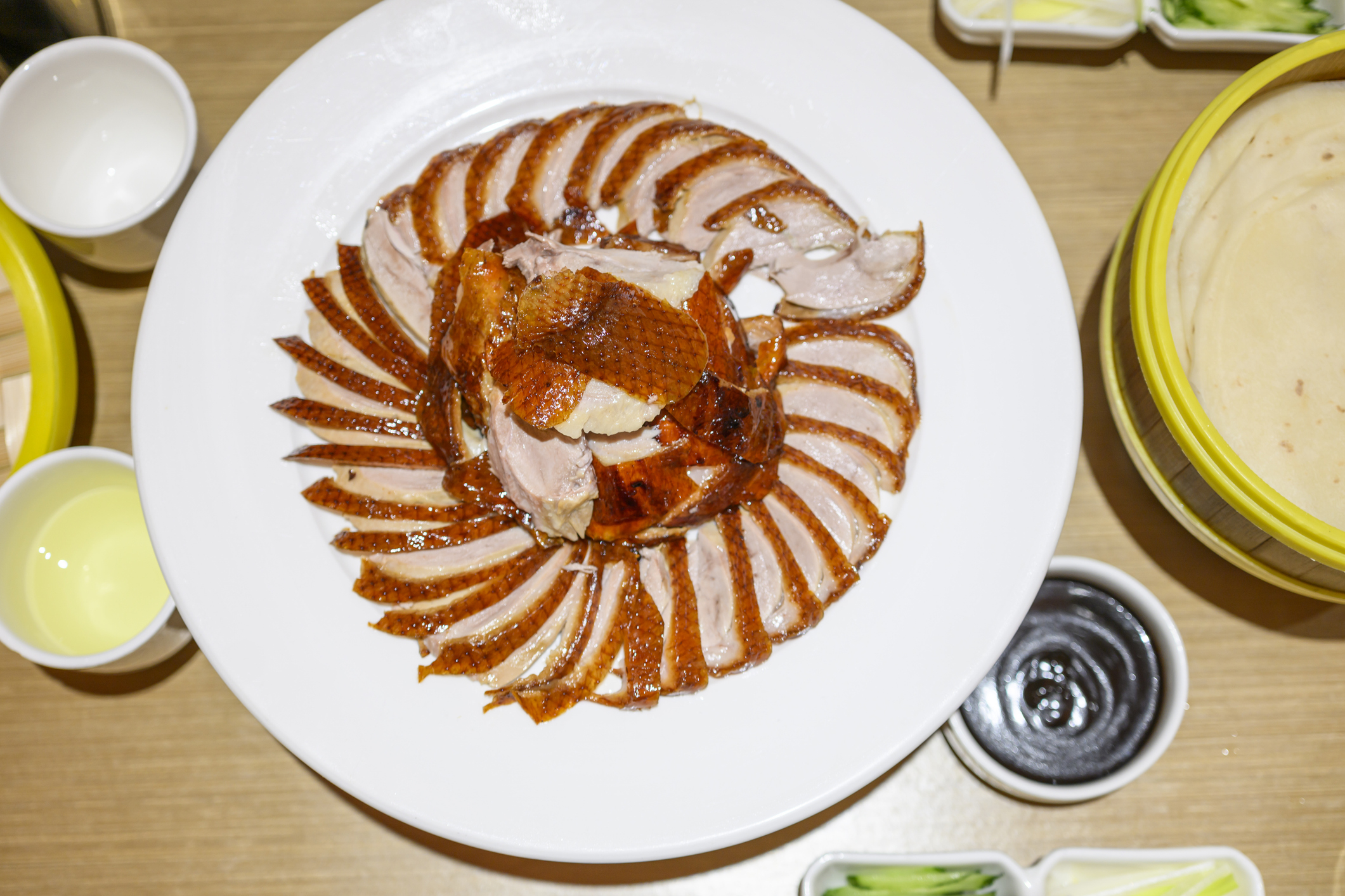 Sliced Peking duck on a plate with condiments and pancakes around it, ready for serving