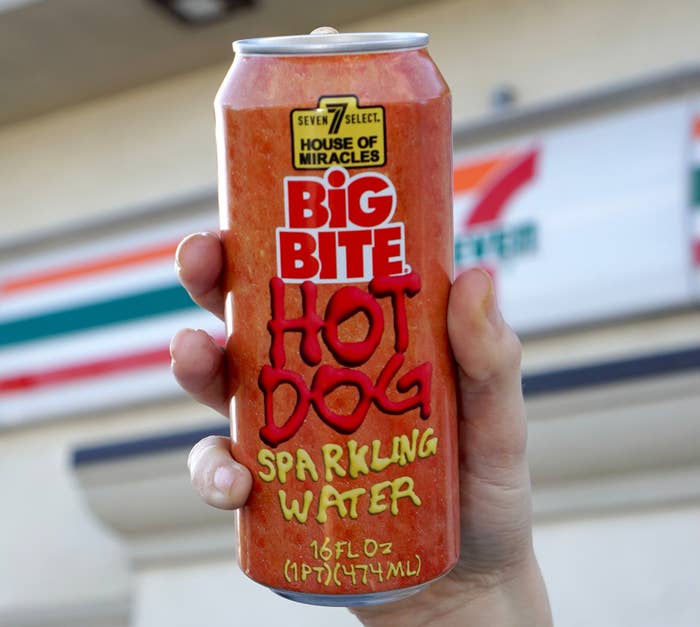 A hand holds a can labeled &quot;BIG BITE HOT DOG Sparkling Water&quot; against a blurred background