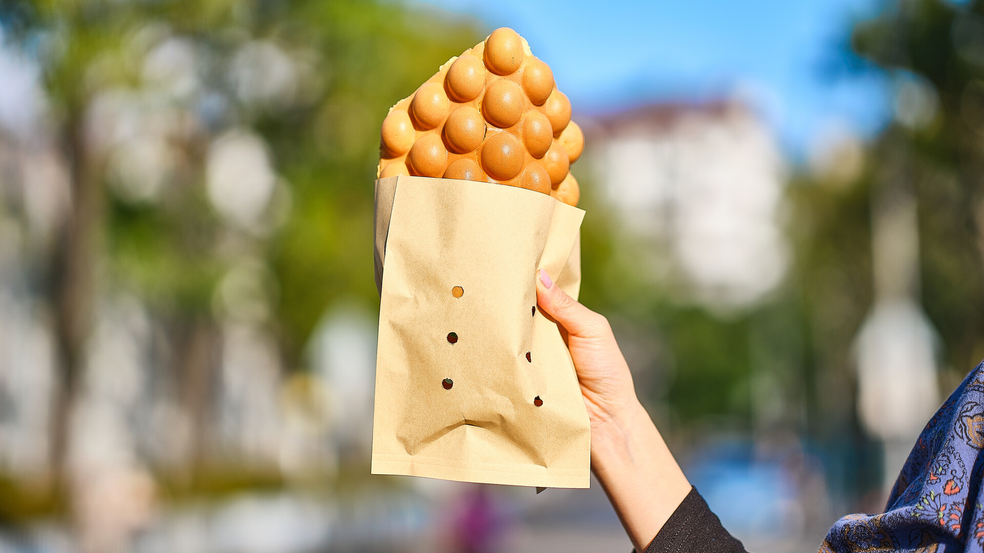 Hand holding a paper cone filled with bubble waffles, outdoor background