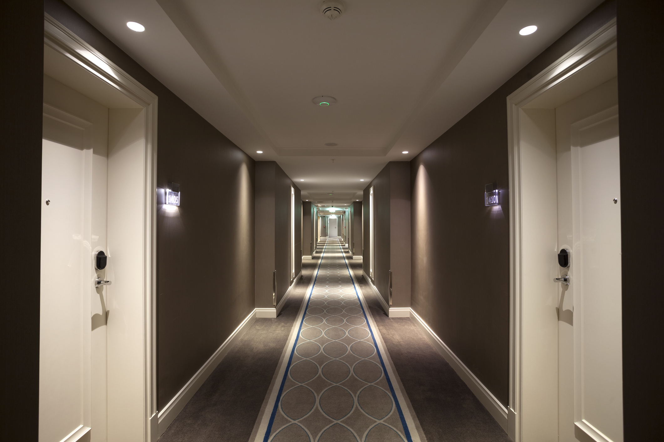 Hotel corridor with patterned carpet leading to intersecting hallway; doors on both sides