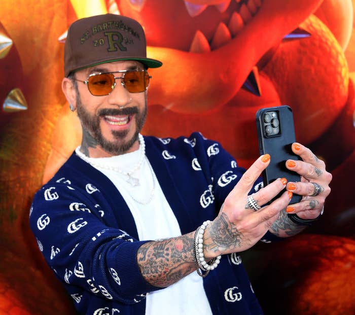 Man in a patterned cardigan and cap taking a selfie with a movie-themed backdrop