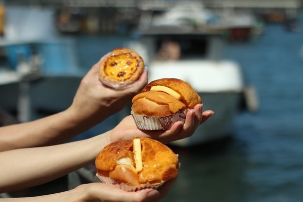 Three hands holding different pastries with a blurred water background