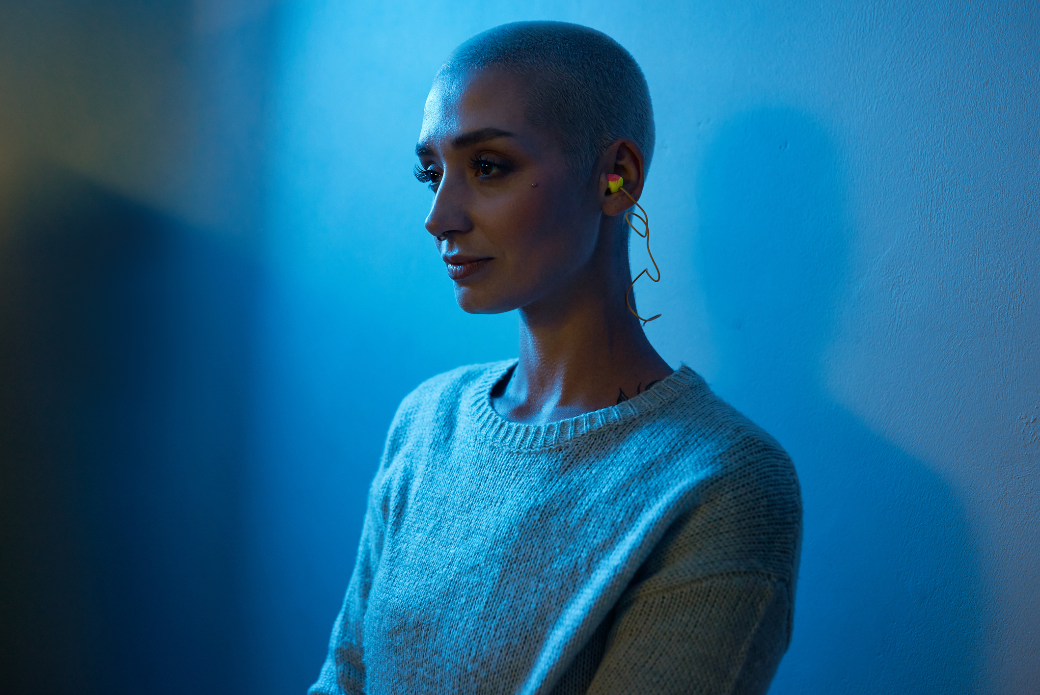 Woman with a buzz cut wearing a sweater and hoop earrings, in side profile with soft lighting