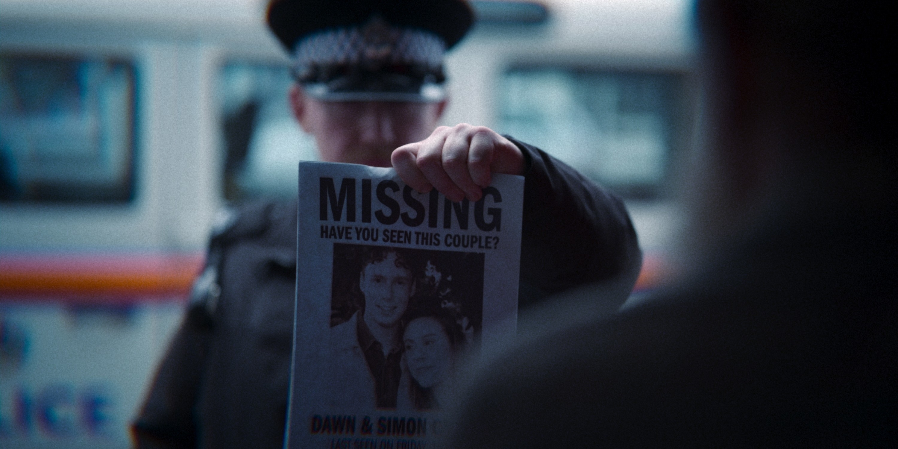 Flyer with &quot;MISSING&quot; text and a photo of a man and woman, held by a person with a police officer in the background