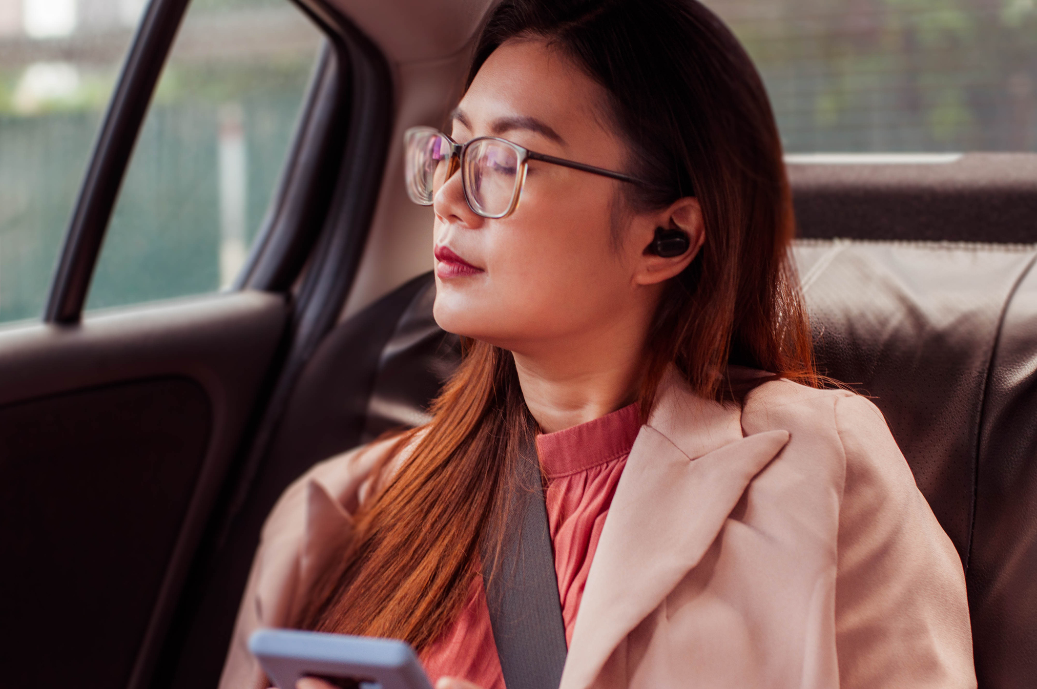 Woman with glasses in car using smartphone, dressed in a professional outfit