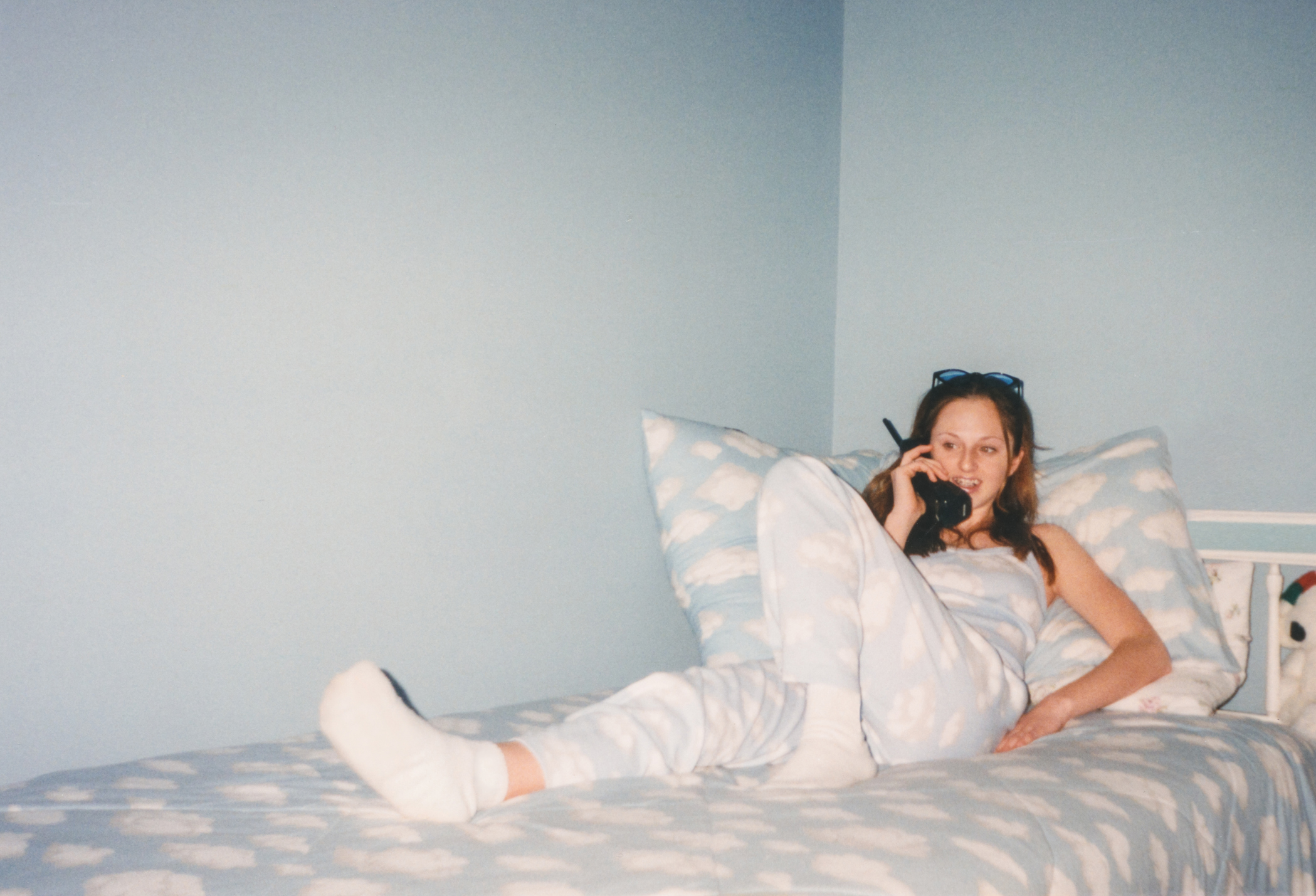 Person relaxing on bed with patterned sheets, talking on a corded phone, evoking a retro vibe